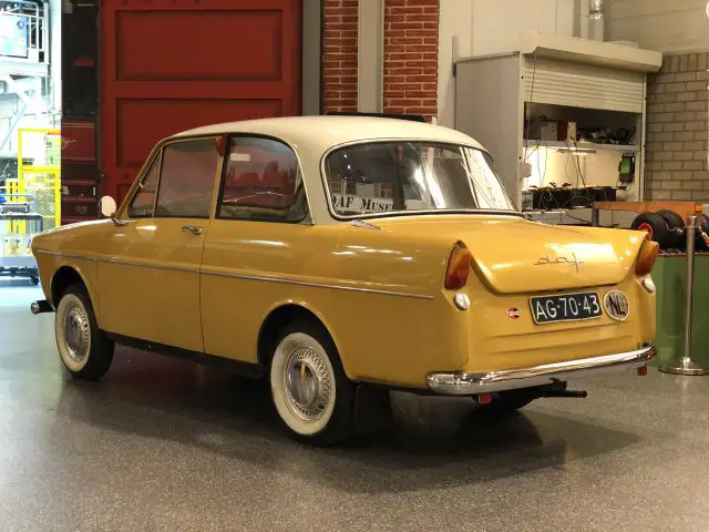 In een garage staat een oude gele auto uit het DAF Museum geparkeerd.