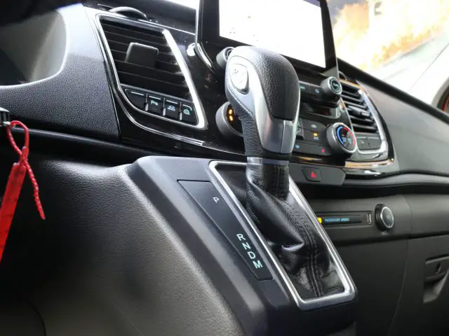 Binnenaanzicht van een Ford Transit Custom MS-RT met de versnellingspook, het multimediasysteemscherm en de dashboardbedieningen.