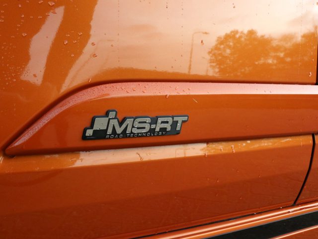 Oranje Ford Transit Custom met een 'MS-RT road technology'-badge op het zijpaneel.