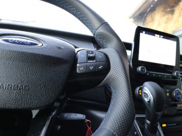 Binnenaanzicht van een Ford Transit Custom MS-RT-voertuig, met de nadruk op de stuurbediening met een dashboardscherm op de achtergrond.