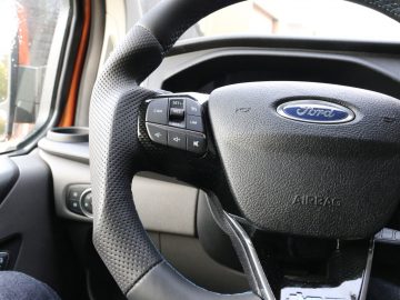 Stuur met gemonteerde bedieningselementen in het interieur van een Ford Transit Custom MS-RT-voertuig.
