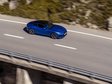 Een blauwe Jaguar F-Type sportwagen die over een bergweg rijdt.