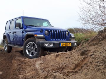 Een blauwe Wrangler rijdt over een onverharde weg.