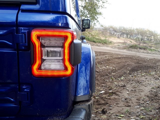 De achterkant van een blauwe Jeep Wrangler op een onverharde weg.