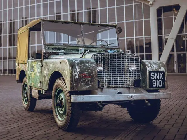 Een oude groene Land Rover 1948 geparkeerd voor een gebouw.