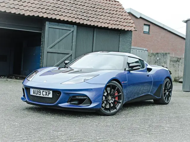 Een blauwe Lotus Evora GT410 Sport geparkeerd voor een garage.