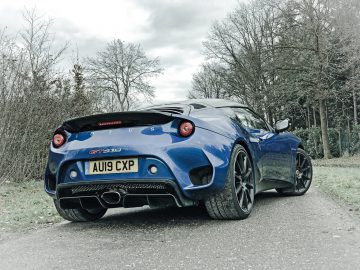 Een blauwe Lotus Evora GT410 Sport staat geparkeerd op een weg.