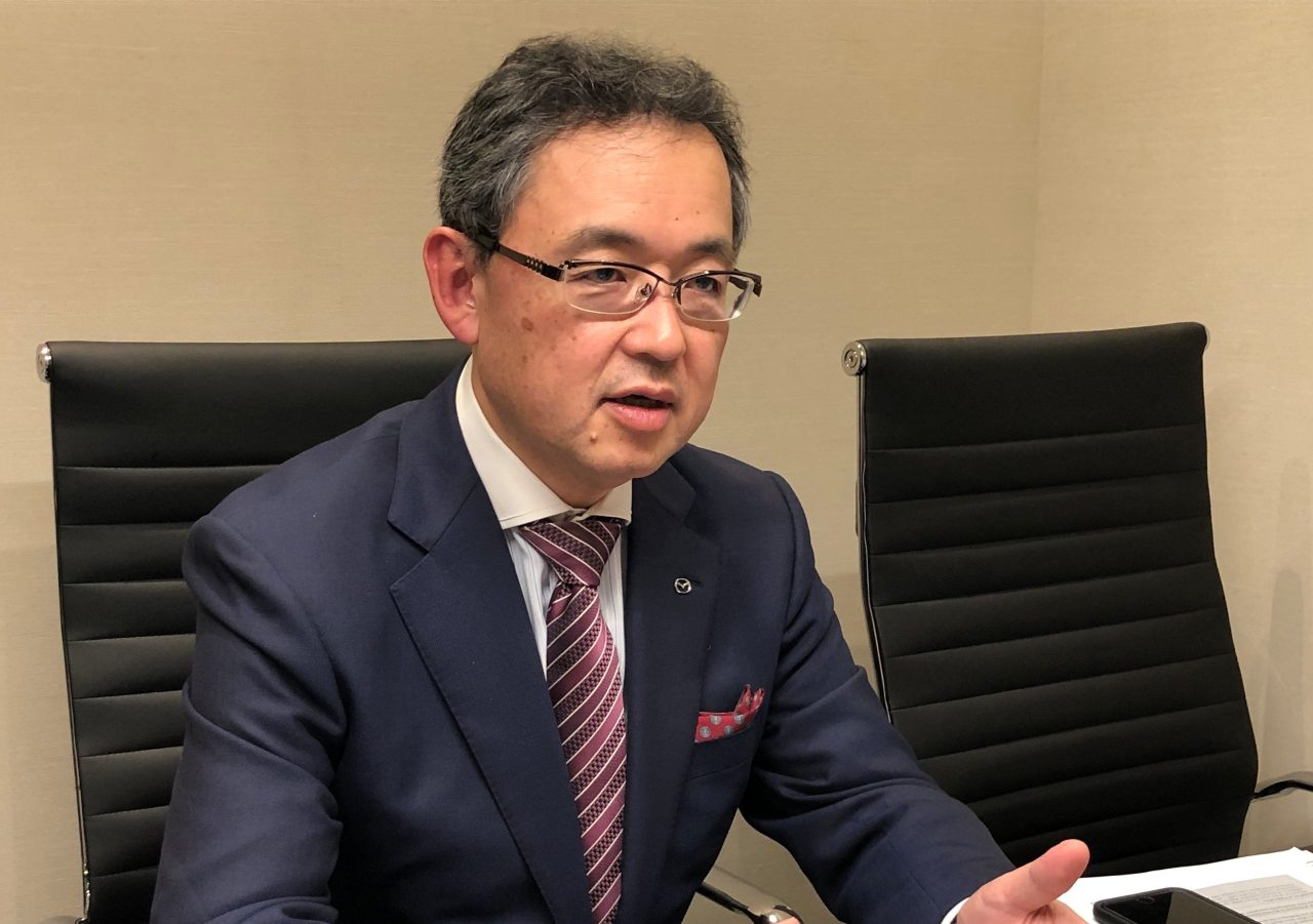 Een man in een Mazda-pak zit aan een bureau.