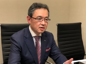 Een man in een Mazda-pak zit aan een bureau.