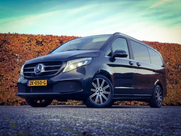 Een zwarte Mercedes-Benz V-Klasse bestelwagen geparkeerd voor een heg.
