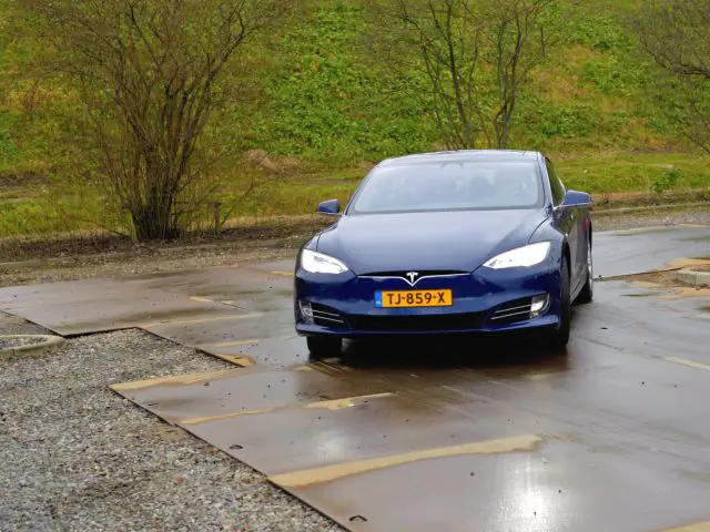 Een blauwe Tesla Model S geparkeerd op een natte weg, te zien in het jaaroverzicht auto's 2019.