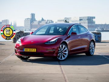 De Tesla Model 3, Auto van het Jaar, staat geparkeerd voor een stad.