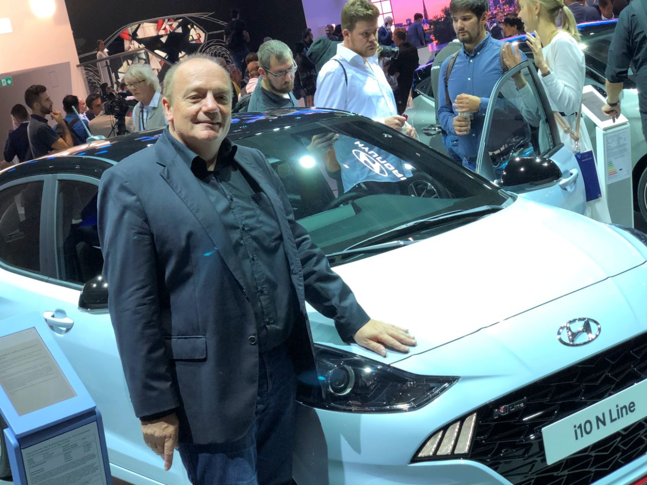 Een man die naast een witte Hyundai i10 staat op een autoshow.