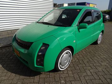 Een groene Toyota Will Cypha parkeerde voor een gebouw.