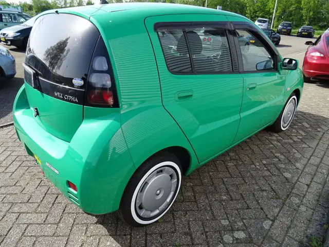 Een kleine groene Toyota Will Cypha geparkeerd op een parkeerplaats.