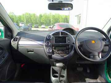 Het interieur van een kleine Toyota Will Cypha met stuur en dashboard.