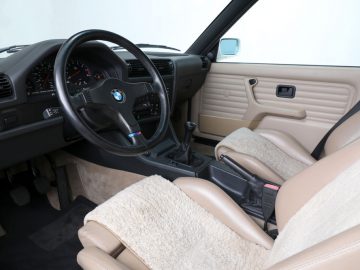 Binnenaanzicht van een klassiek BMW-voertuig, dat doet denken aan het type uit The Fast and the Furious, met de bestuurdersstoel, het stuur en het dashboard.