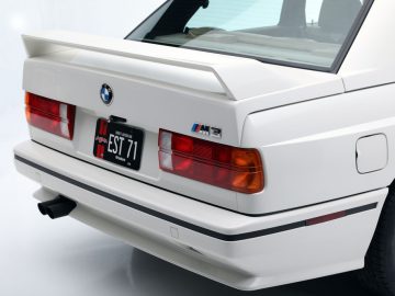 Achteraanzicht van een witte BMW M3 met de achterlichten en het kofferbaklogo, dat doet denken aan de serie "The Fast and the Furious".