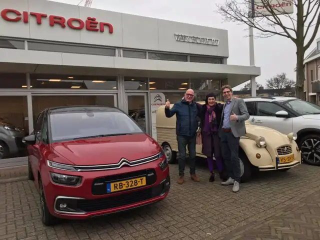 Drie mensen poseren met hun duimen omhoog voor een rode auto bij een Citroën-dealer.