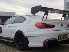 Witte BMW M6 GT3 met een aftermarket-achtervleugel geparkeerd buiten bij een gebouw met het M Power-logo.