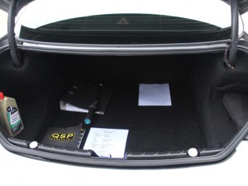 Open de kofferbak van de BMW M6 GT3 met daarin een fles motorolie, een zwarte tas en wat papierwerk.