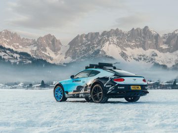 Een luxe Bentley Continental Ice GT-sportwagen met imperiaal geparkeerd op een besneeuwde vlakte met bergen op de achtergrond in de schemering.