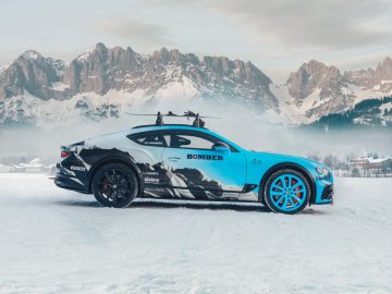 Een Bentley Continental Ice GT-sportwagen met een snowboardrek geparkeerd in de sneeuw tegen een bergachtergrond.