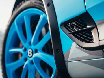 Close-up van het stuur en de ventilatieopening aan de zijkant van een blauwe sportwagen, met een Bentley Continental Ice GT-logo.