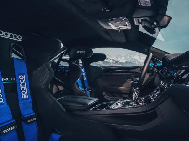 Binnenaanzicht van een Bentley Continental Ice GT met blauwe Sparco-raceharnassen en een bergachtige achtergrond zichtbaar door het raam.