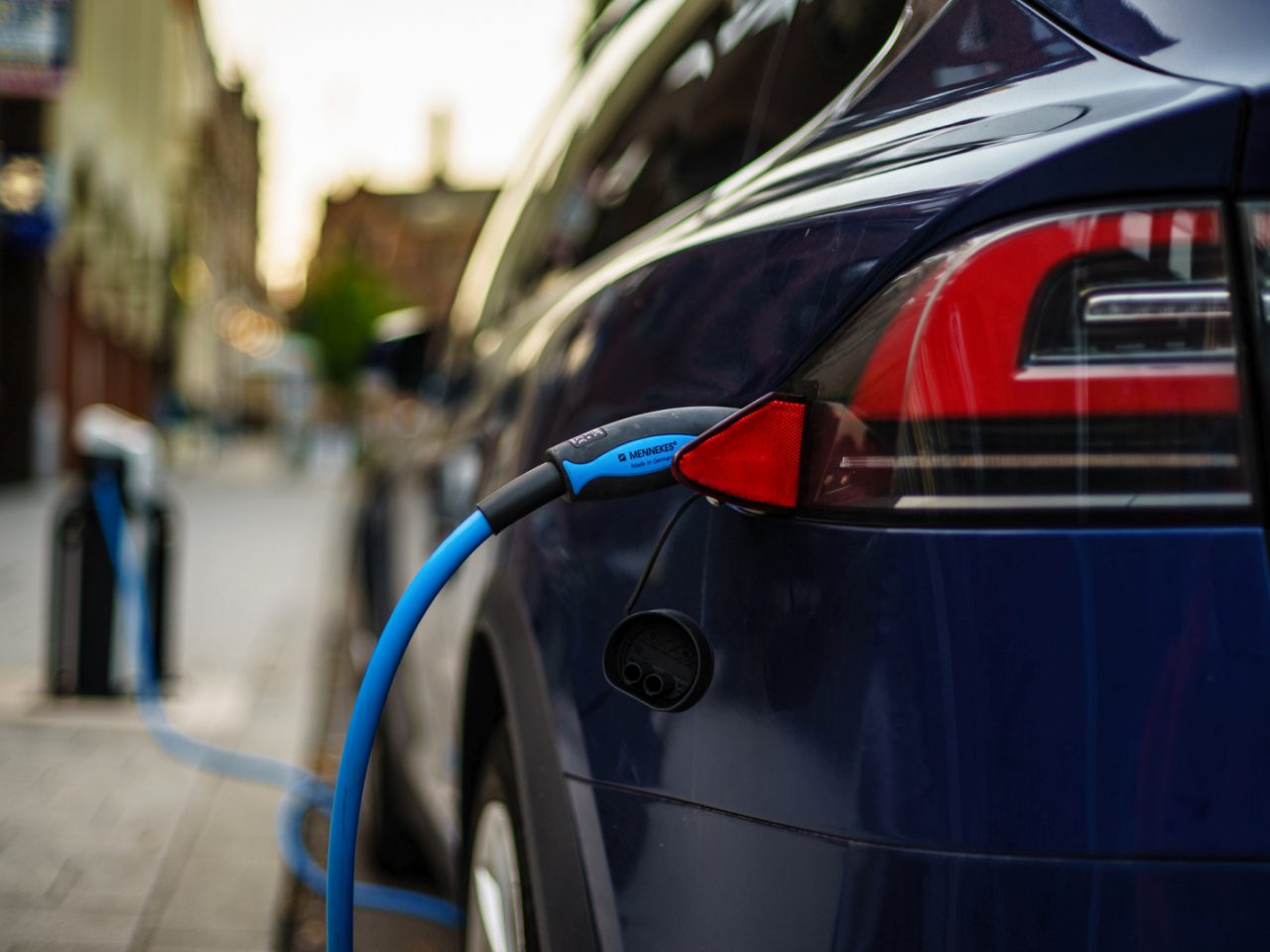 Een elektrische auto wordt opgeladen bij een laadpaal aan de straatkant voor "elektrische auto verborgen".