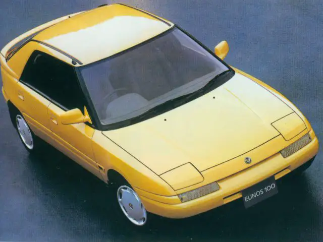 Gele Mazda eunos 100 hatchback-auto vanuit een hoek.