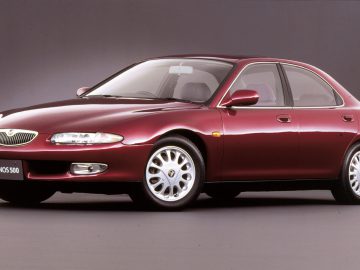 Een rode Mazda Eunos 500 sedan tegen een grijze achtergrond.