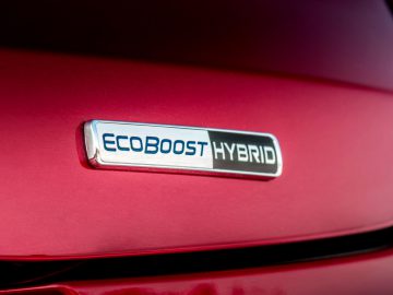 Close-up van een "Ford Puma Ecoboost Hybrid" -badge op een rode auto.