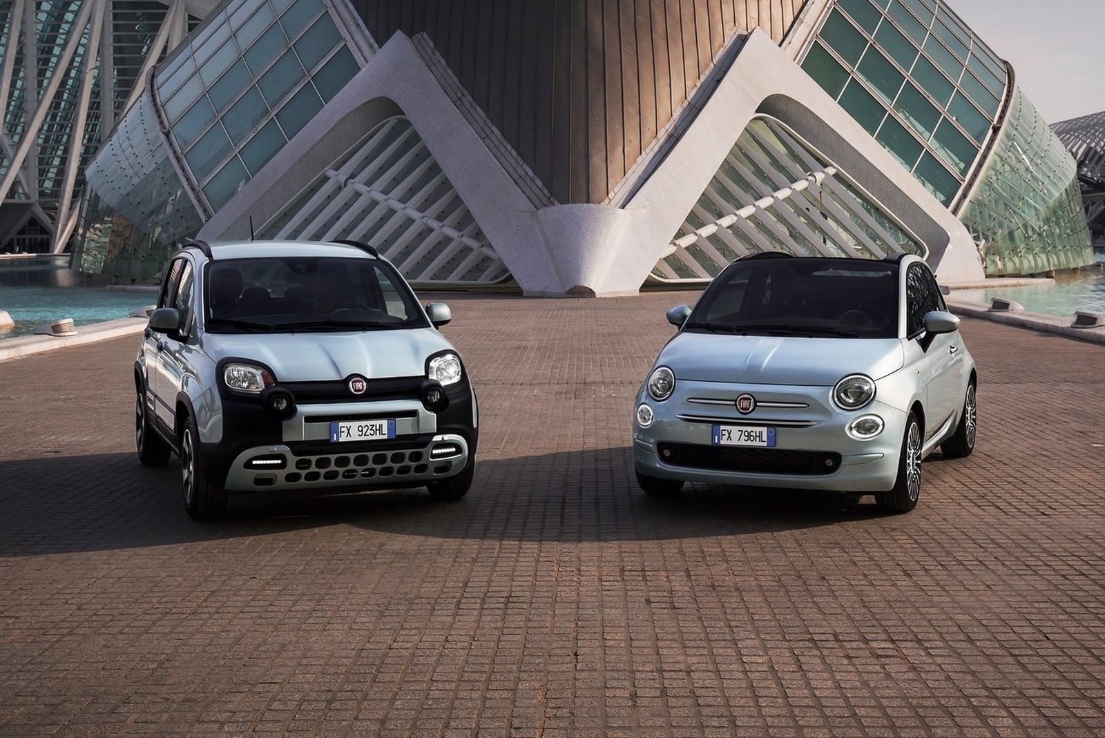 Twee Fiat 500 hybride auto's geparkeerd tegenover elkaar voor een moderne architectonische structuur.