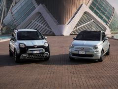 Twee Fiat 500 hybride auto's geparkeerd tegenover elkaar voor een moderne architectonische structuur.