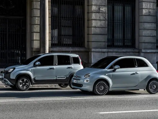 Twee compacte Fiat 500 hybride auto's geparkeerd in een stadsstraat, met een moderne gevel van een gebouw op de achtergrond.