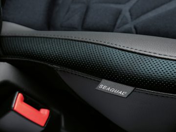 Close-up van een Fiat 500 Hybrid-autostoeltje met Seaqual®-logo, met een gestructureerd zwart lederen ontwerp en een rode veiligheidsgordelgesp.