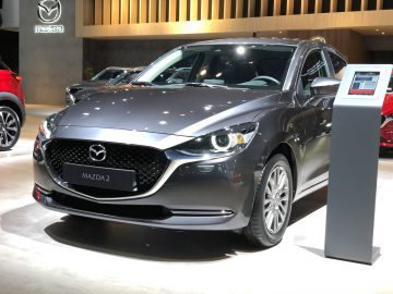 Een Mazda2-auto tentoongesteld op de tentoonstelling Autosalon van Brussel 2020 met een informatiestand ernaast.