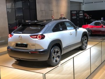 Een witte elektrische Mazda MX-30, tentoongesteld op het Autosalon van Brussel 2020, met toeschouwers op de achtergrond.
