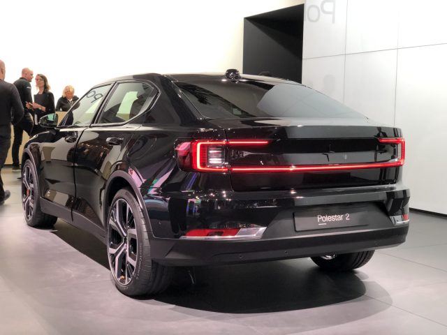 Een zwarte elektrische Polestar 2-auto tentoongesteld op het Autosalon van Brussel 2020 met bezoekers op de achtergrond.