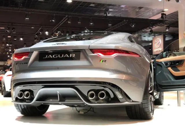 Een zilveren Jaguar F-Type R-sportwagen tentoongesteld op het Autosalon van Brussel 2020, gezien vanuit een achterhoek, met de nadruk op de quad-uitlaten en het sportieve ontwerp.