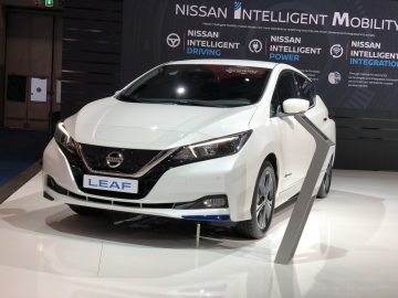 Een witte elektrische auto van de Nissan Leaf, tentoongesteld op het Autosalon van Brussel 2020 met promotiebanners op de achtergrond.