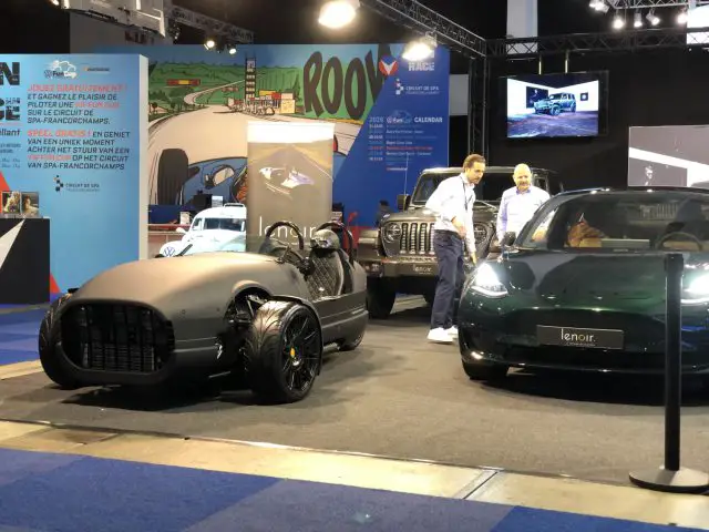 Twee individuen die praten naast een auto in vintagestijl en een moderne elektrische auto op de autotentoonstelling van Brussels Motor Show 2020.