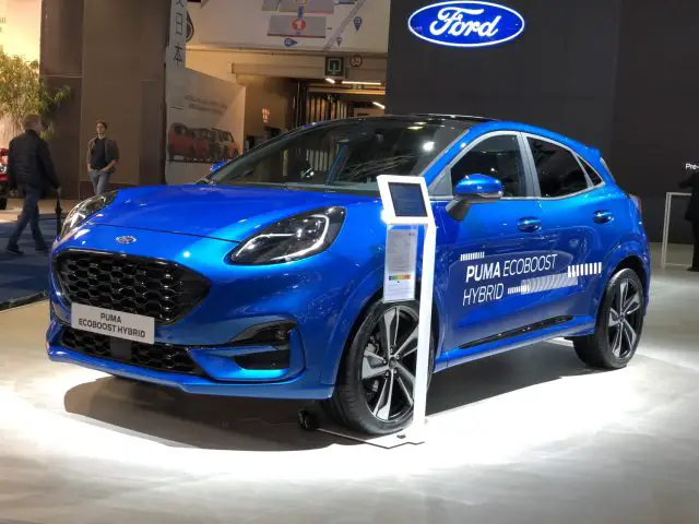 Blauwe Ford Puma EcoBoost Hybrid tentoongesteld op het Autosalon van Brussel 2020, vergezeld van een informatiebord.