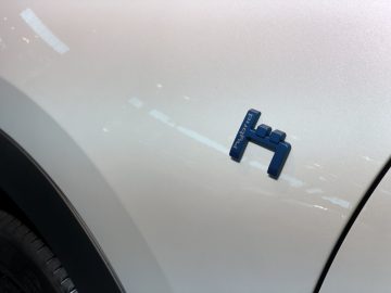 Close-up van een zilveren auto met een blauwe 'hybride' badge bij het voorwiel, tentoongesteld op het Autosalon van Brussel 2020.