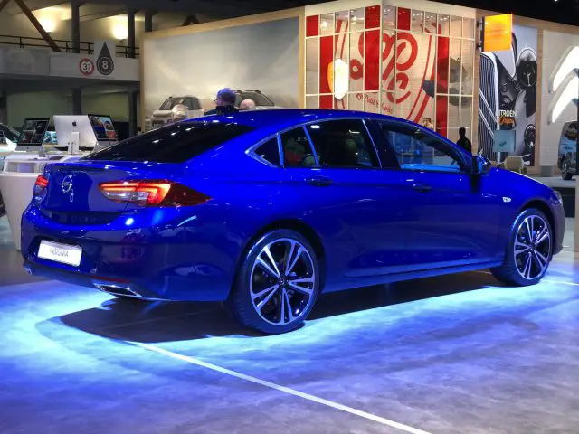 Een blauwe sedan, tentoongesteld op het Autosalon van Brussel 2020, met een strak design en lichtmetalen velgen.