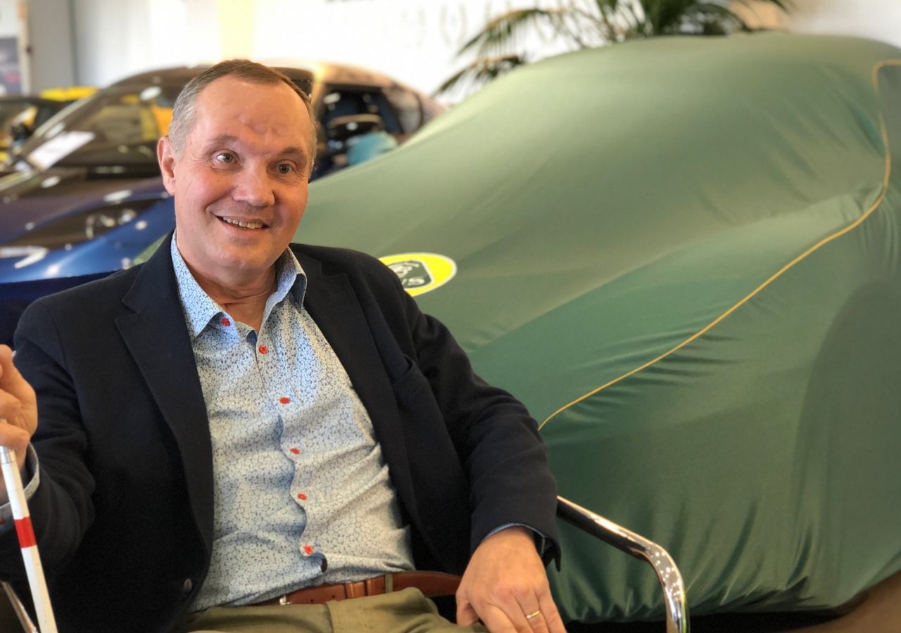 Man zit in een showroom met een overdekte Lotus op de achtergrond.