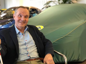 Man zit in een showroom met een overdekte Lotus op de achtergrond.