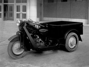 Een vintage Mazda-motorfiets op drie wielen met een laadbak geparkeerd voor een gebouw.