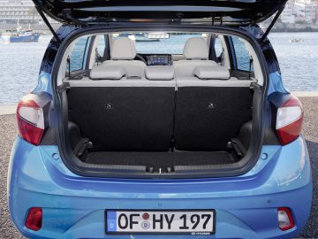 Achteraanzicht van een Hyundai i10 blauwe hatchback-auto met open kofferbak, waardoor de laadruimte zichtbaar is.